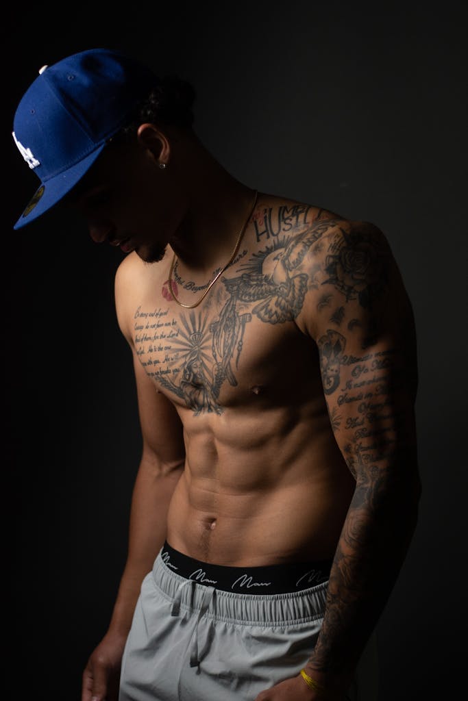 A shirtless man with tattoos and a blue hat